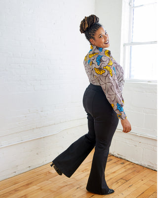 Woman in a patterned shirt and black pants standing in a room with white walls and wooden floor.  These pants are the Ashwood Pants sewing pattern from Cashmerette.