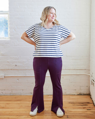 Woman wearing a striped shirt and purple pants standing in a room with white brick walls and wooden floor. These pants are the Ashwood Pants sewing pattern from Cashmerette.