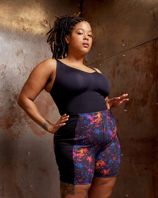 Person wearing a black tank top and colorful shorts standing against a textured wall. These shorts are the Wickham Shorts sewing pattern from Cashmerette.