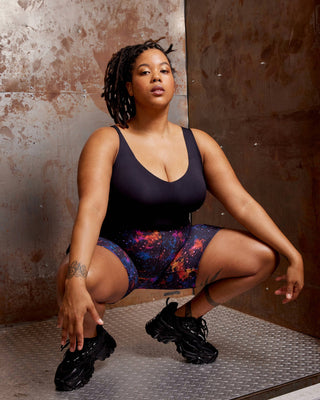 Woman squatting in a black tank top and colorful shorts against a textured wall. These shorts is the Wickham Shorts sewing pattern from Cashmerette.