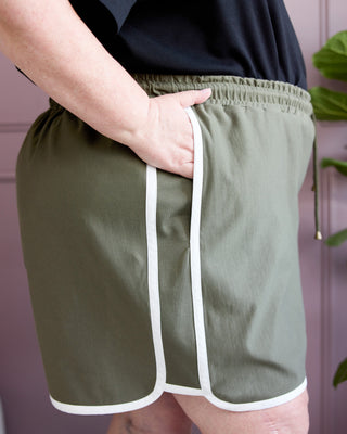 Person wearing green shorts with white trim against a pink background. This is the Rowley Shorts sewing pattern from Cashmerette.