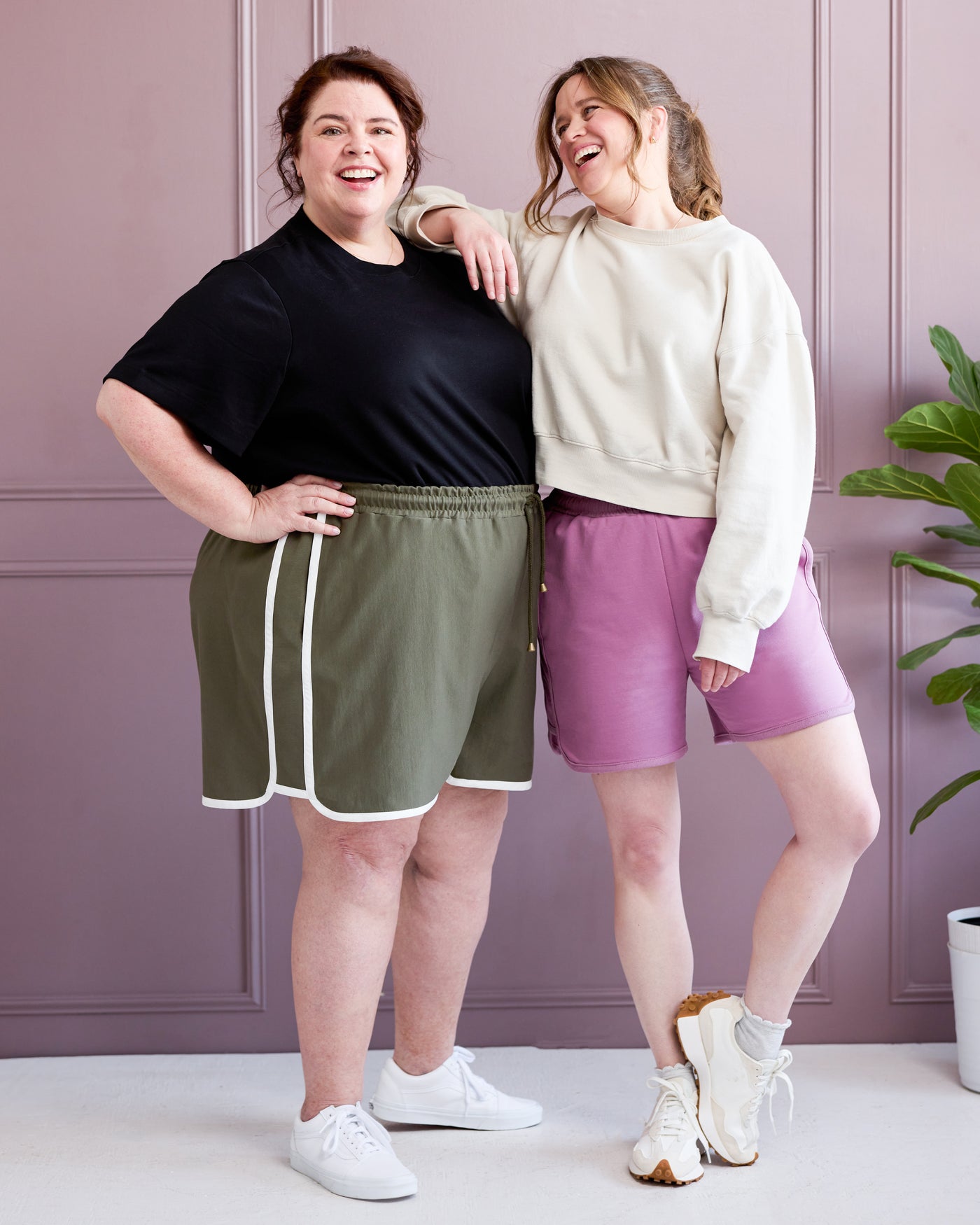 Two women standing together wearing athletic wear against a light purple wall. This is the Rowley Shorts sewing pattern from Cashmerette.