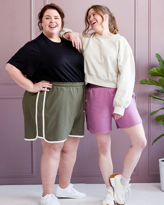 Two women standing together wearing athletic wear against a light purple wall.