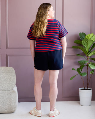 Person wearing a striped shirt and shorts standing in a room with a plant and chair. This is the Rowley Shorts sewing pattern from Cashmerette.