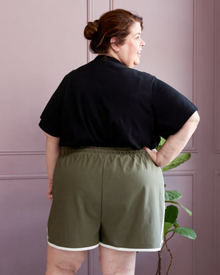 Person wearing a black shirt and green shorts against a purple wall. This is the Rowley Shorts sewing pattern from Cashmerette.