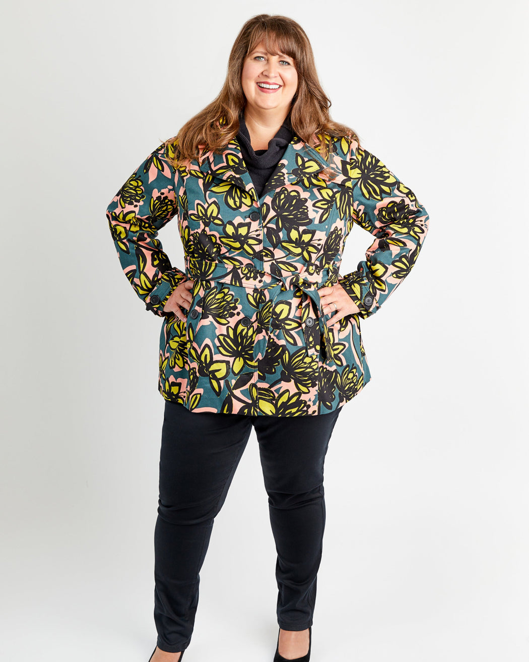 Woman wearing a colorful floral jacket on a white background. This coat is the Chilton Trench Coat sewing pattern from Cashmerette.
