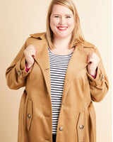 Woman wearing a tan coat over a striped shirt on a beige background. This coat is the Chilton Trench Coat sewing pattern from Cashmerette.