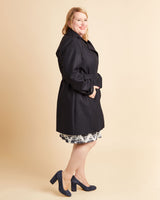 Woman wearing a black coat on a beige background. This coat is the Chilton Trench Coat sewing pattern from Cashmerette.