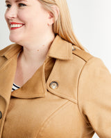 Woman wearing a tan coat on a plain background. This coat is the Chilton Trench Coat sewing pattern from Cashmerette.
