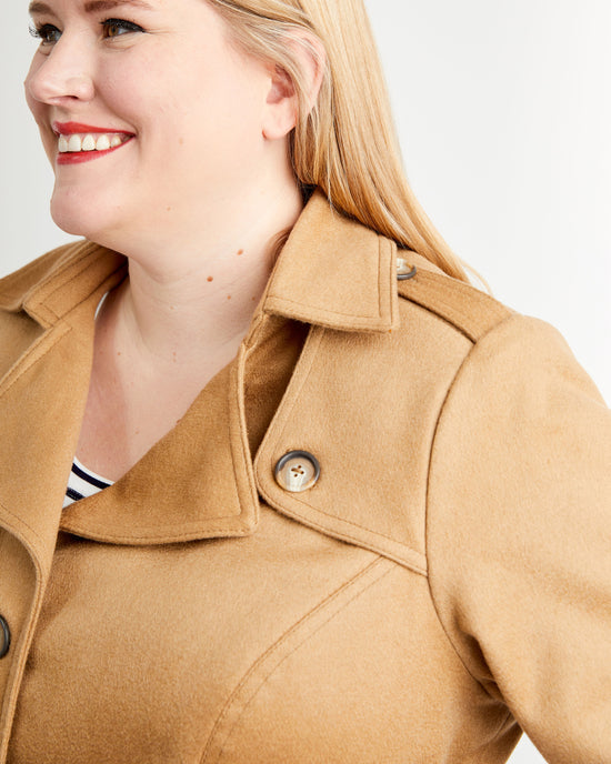 Woman wearing a tan coat on a plain background. This coat is the Chilton Trench Coat sewing pattern from Cashmerette.