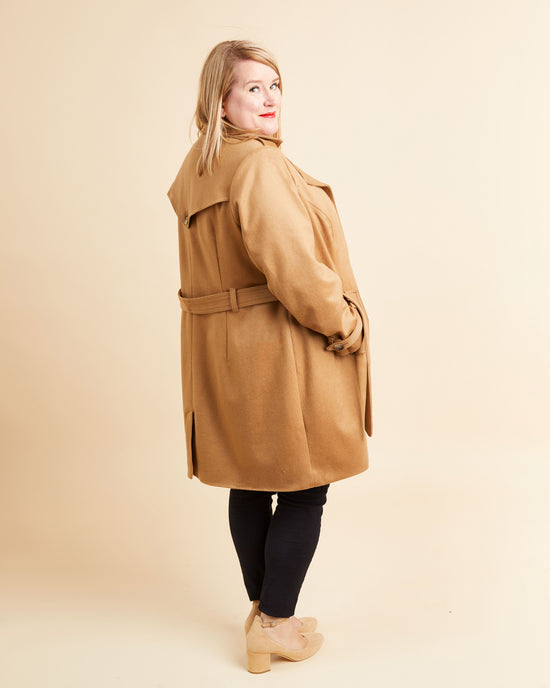 Woman wearing a tan coat on a beige background. This coat is the Chilton Trench Coat sewing pattern from Cashmerette.