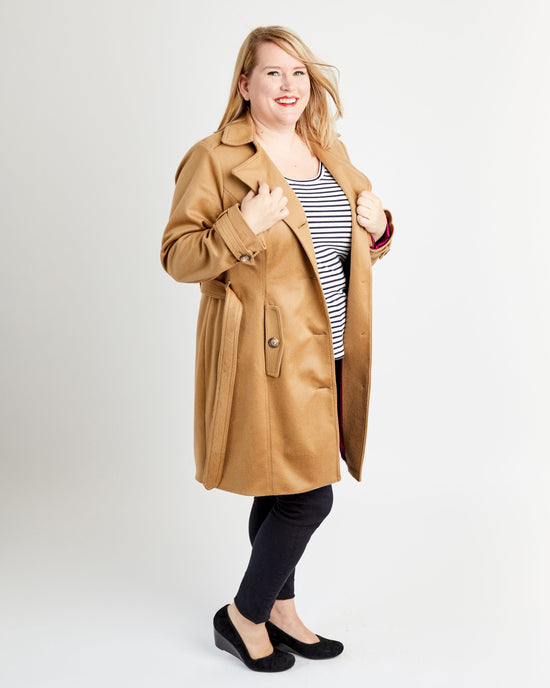 Woman wearing a tan coat over a striped shirt on a white background. This coat is the Chilton Trench Coat sewing pattern from Cashmerette.