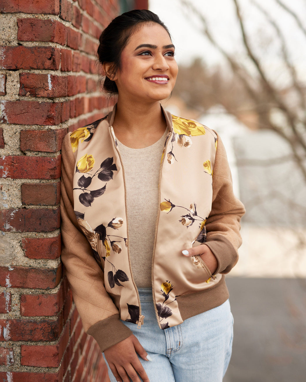 Woman wearing a floral bomber jacket leaning against a brick wall. This jacket is the Cashmerette Club Kimball Bomber Jacket sewing pattern.