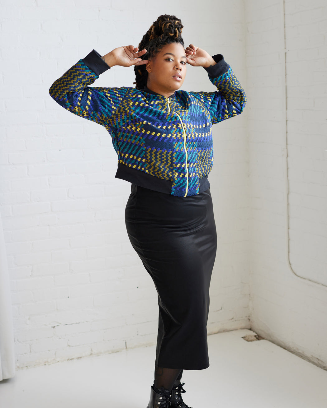 Person wearing a patterned blue and green sweater with a black skirt against a white wall. This jacket is the Cashmerette Club Kimball Bomber Jacket sewing pattern.