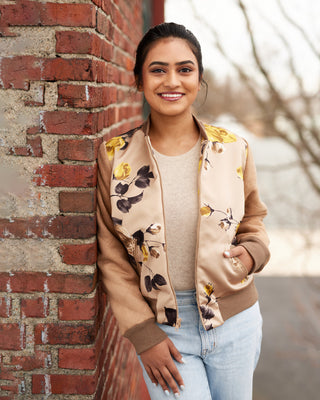 Woman wearing a floral bomber jacket leaning against a brick wall. This jacket is the Cashmerette Club Kimball Bomber Jacket sewing pattern.