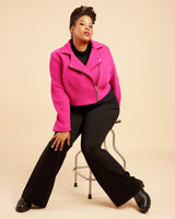 Person wearing a bright pink jacket and black pants on a beige background. This biker jacket is the Canton Moto Jacket sewing pattern from Cashmerette.