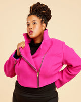 Person wearing a bright pink jacket and black pants on a beige background. This biker jacket is the Canton Moto Jacket sewing pattern from Cashmerette.