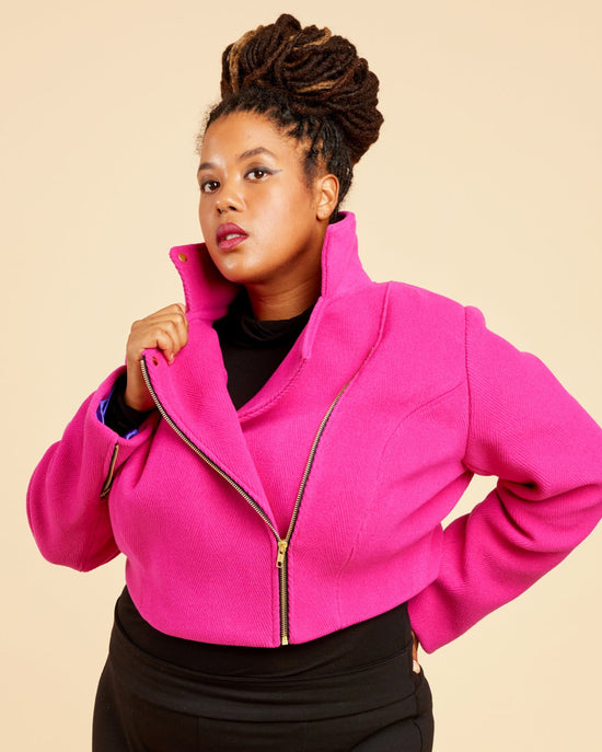 Person wearing a bright pink jacket and black pants on a beige background. This biker jacket is the Canton Moto Jacket sewing pattern from Cashmerette.