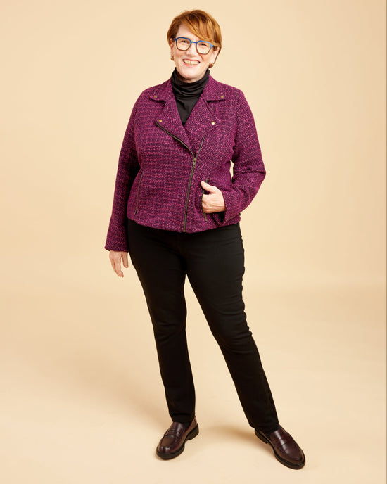 Woman wearing a purple jacket and black pants on a beige background. This biker jacket is the Canton Moto Jacket sewing pattern from Cashmerette.