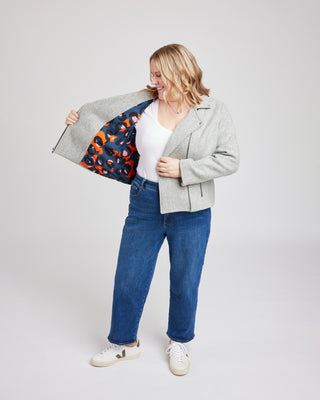 Person wearing a gray jacket with a colorful lining, white shirt, blue jeans, and white sneakers on a light gray background. This biker jacket is the Canton Moto Jacket sewing pattern from Cashmerette.