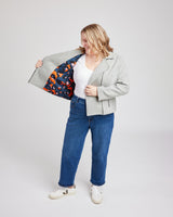 Person wearing a gray jacket with a colorful lining, white shirt, blue jeans, and white sneakers on a light gray background. This biker jacket is the Canton Moto Jacket sewing pattern from Cashmerette.