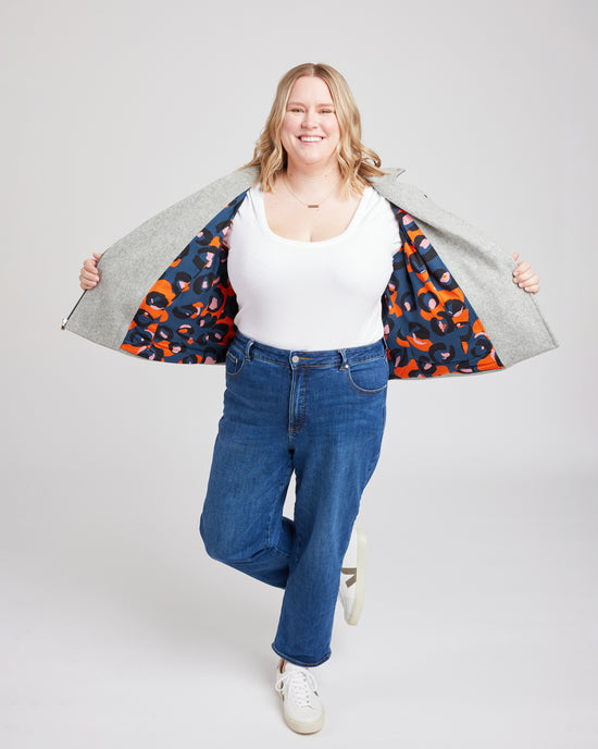 Woman wearing a white top, blue jeans, and a colorful jacket over her shoulders on a plain background. This biker jacket is the Canton Moto Jacket sewing pattern from Cashmerette.