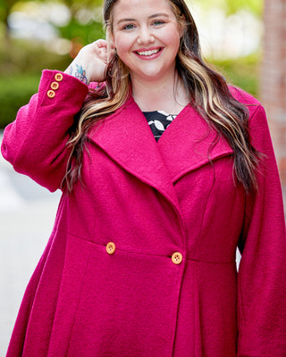Woman wearing a bright pink coat with gold buttons outdoors. This coat is the Savin Coat sewing pattern from Cashmerette.
