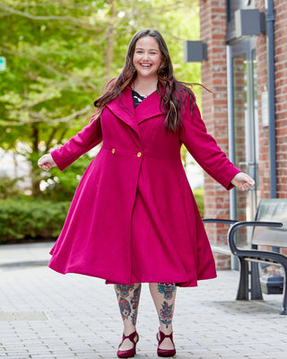 Woman wearing a bright pink coat standing outdoors on a sunny day. This coat is the Savin Coat sewing pattern from Cashmerette.