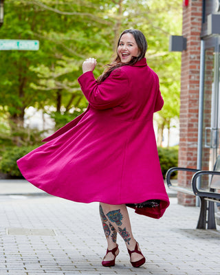 Person wearing a bright pink coat outdoors on a sunny day. This coat is the Savin Coat sewing pattern from Cashmerette.