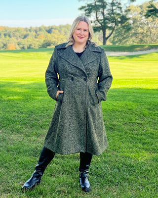 Woman wearing a gray coat standing in a grassy field with trees in the background. This coat is the Savin Coat sewing pattern from Cashmerette.