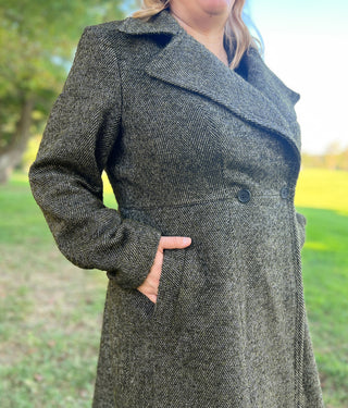 Person wearing a long dark coat outdoors with greenery in the background. This coat is the Savin Coat sewing pattern from Cashmerette.