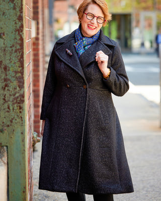 Woman wearing a dark coat and glasses standing on a street. This coat is the Savin Coat sewing pattern from Cashmerette.