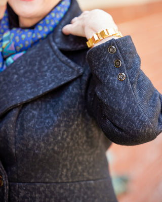 Close-up of a person wearing a dark coat with buttons, a colorful scarf, and a gold watch. This coat is the Savin Coat sewing pattern from Cashmerette.