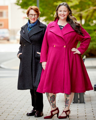 Two women standing on a street, one in a black coat and the other in a pink coat. This coat is the Savin Coat sewing pattern from Cashmerette.