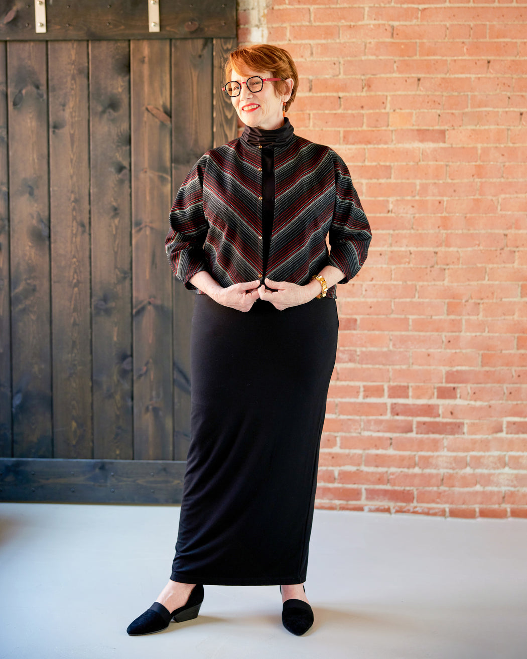 Person wearing a striped sweater and black skirt against a brick wall. This jacket is the Catskills Bias Jacket sewing pattern from Cashmerette.