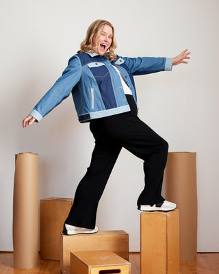 Person wearing a blue jacket and black pants standing on wooden boxes against a white wall. This jacket is the Glover Jean Jacket sewing pattern from Cashmerette.