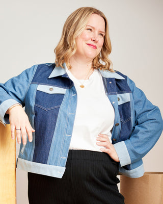 Woman wearing a blue denim jacket over a white shirt, standing next to wooden boxes. This jacket is the Glover Jean Jacket sewing pattern from Cashmerette.
