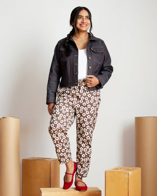 Woman in floral pants and denim jacket standing on cardboard boxes against a white background. This jacket is the Glover Jean Jacket sewing pattern from Cashmerette.