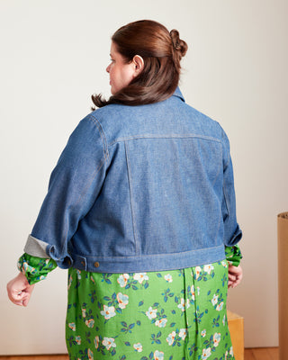 Person wearing a blue denim jacket over a green floral dress on a plain background, This jacket is the Glover Jean Jacket sewing pattern from Cashmerette.