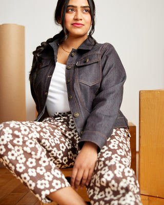 Woman wearing a denim jacket and floral pants sitting on a wooden floor. This jacket is the Glover Jean Jacket sewing pattern from Cashmerette.
