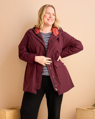 Woman wearing a burgundy jacket with a striped shirt and black pants against a beige background.  This is the Marston Raincoat sewing pattern from Cashmerette Club.