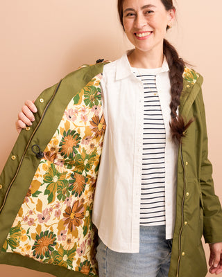 Woman wearing a green jacket with a floral pattern on a beige background. This is the Marston Raincoat sewing pattern from Cashmerette Club.