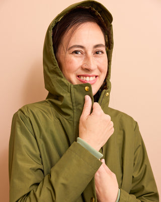 Woman wearing a green raincoat against a beige background. This is the Marston Raincoat sewing pattern from Cashmerette Club.