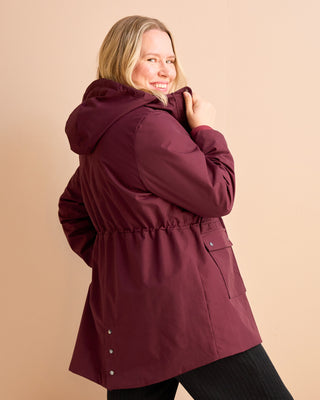 Woman wearing a burgundy parka against a beige background. This is the Marston Raincoat sewing pattern from Cashmerette Club.