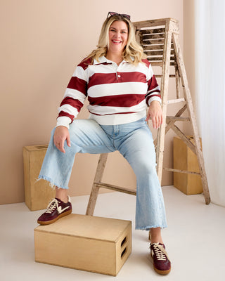 Woman sitting on a wooden stool wearing a red and white striped shirt and blue jeans, with a wooden ladder and boxes in the background. This is the Brookhaven Sweatshirt sewing pattern from Cashmerette.