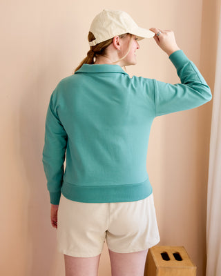 Person wearing a teal jacket and beige cap against a beige background. This is the Brookhaven Sweatshirt sewing pattern from Cashmerette.