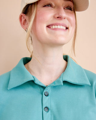 Woman wearing a teal polo shirt and beige hat against a beige background. This is the Brookhaven Sweatshirt sewing pattern from Cashmerette.