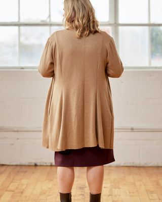 Person wearing a beige cardigan over a dark skirt in a room with large windows. This cardigan is the Westmore Cardigan sewing pattern from Cashmerette.