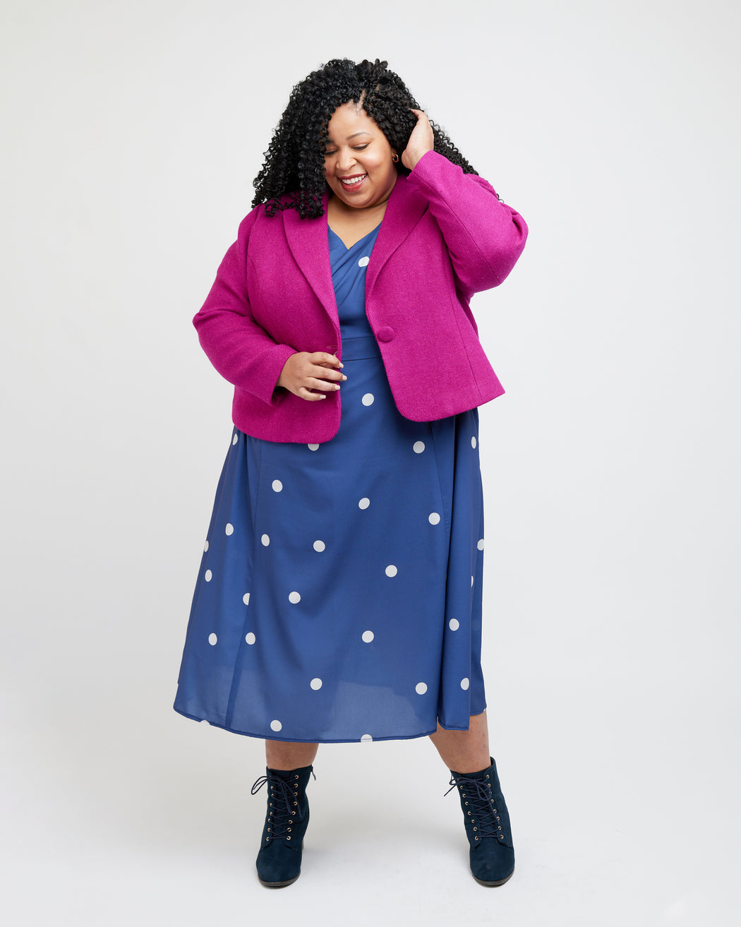 Woman wearing a bright pink coat over a blue dress with white polka dots on a white background. This blazer is the Auburn Blazer sewing pattern from Cashmerette.