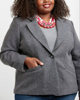 Woman wearing a gray blazer over a gray top with a pink necklace on a white background. This blazer is the Auburn Blazer sewing pattern from Cashmerette.